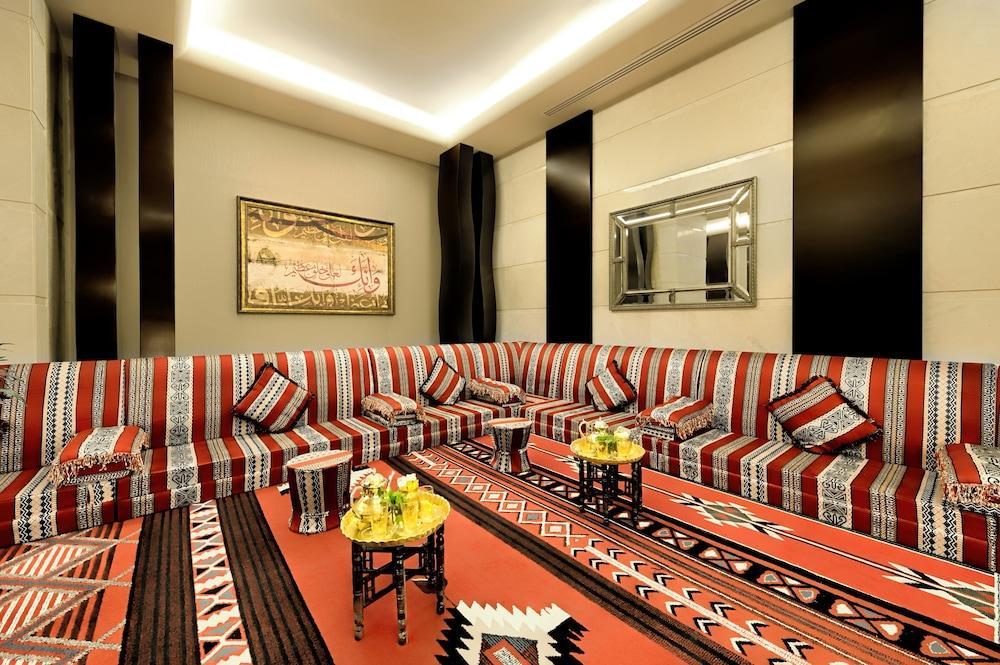 Al Ghufran Safwah Hotel Makkah Mekka Exteriör bild The photo depicts a spacious and elegantly designed living room. The seating area features a large, L-shaped couch adorned with colorful cushions, primarily in red, black, and white patterns. The walls are decorated with sleek, modern finishes, and l