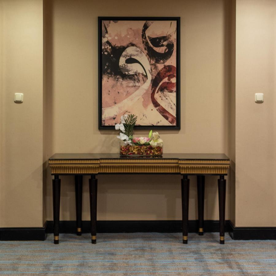 Al Ghufran Safwah Hotel Makkah Mekka Exteriör bild The photo shows a hallway featuring a decorative wall with a large, abstract painting that includes swirls and shapes in shades of pink and cream. Below the painting, there is a wooden console table with dark legs and a striped design. On the table, 