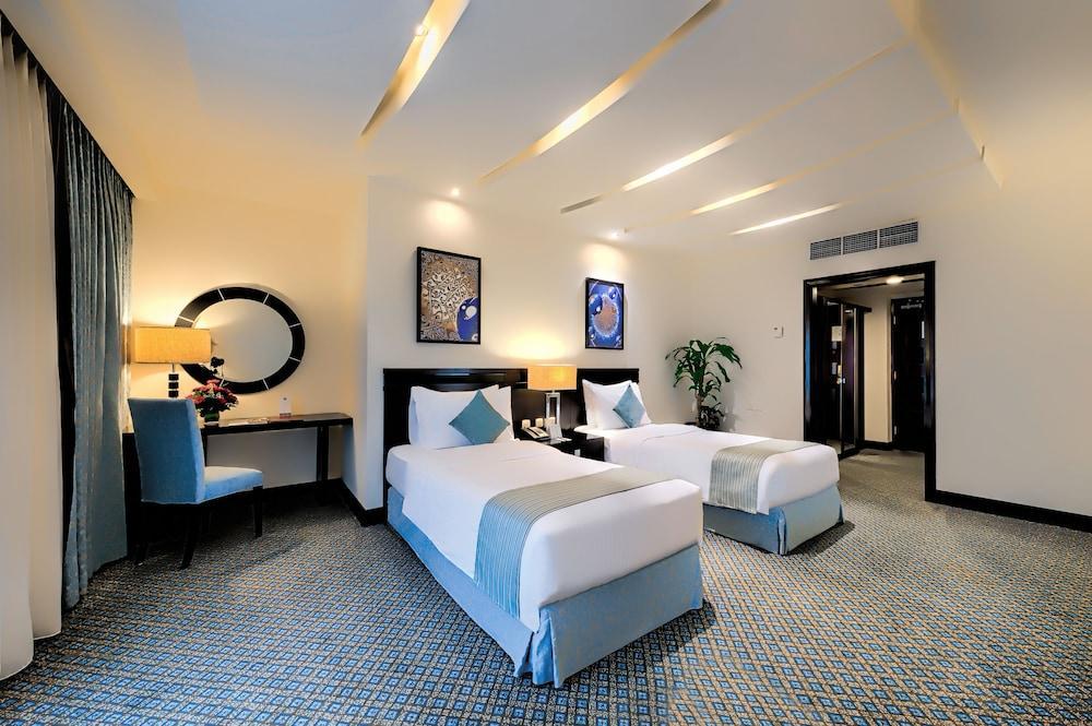 Al Ghufran Safwah Hotel Makkah Mekka Exteriör bild The photo shows a modern hotel room featuring two single beds with light blue accents. There is a decorative piece of artwork on the wall above each bed. A round mirror is also hanging on the wall, complemented by a stylish lamp on a wooden bedside t