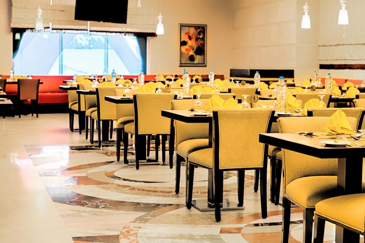 Al Ghufran Safwah Hotel Makkah Mekka Exteriör bild The photo features a dining area with several tables and chairs arranged neatly. The chairs have yellow upholstery, and each table is set with yellow napkins. The flooring has a marble design, and there are decorative elements in the background, incl