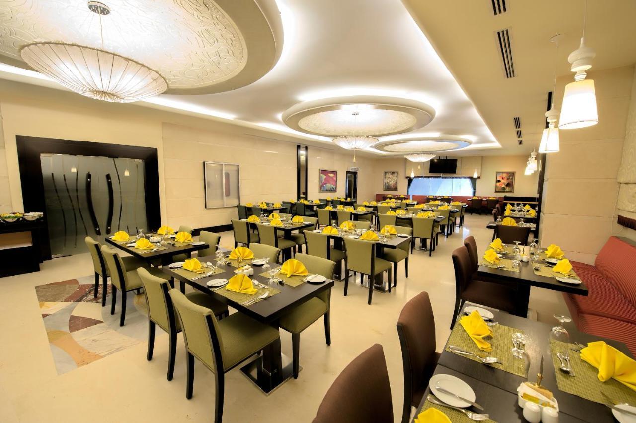 Al Ghufran Safwah Hotel Makkah Mekka Exteriör bild The photo shows the interior of a modern restaurant. The space features neatly arranged tables with dark wooden surfaces and green chairs. Each table is set with yellow napkins, silverware, and glassware, suggesting a prepared dining atmosphere. The 