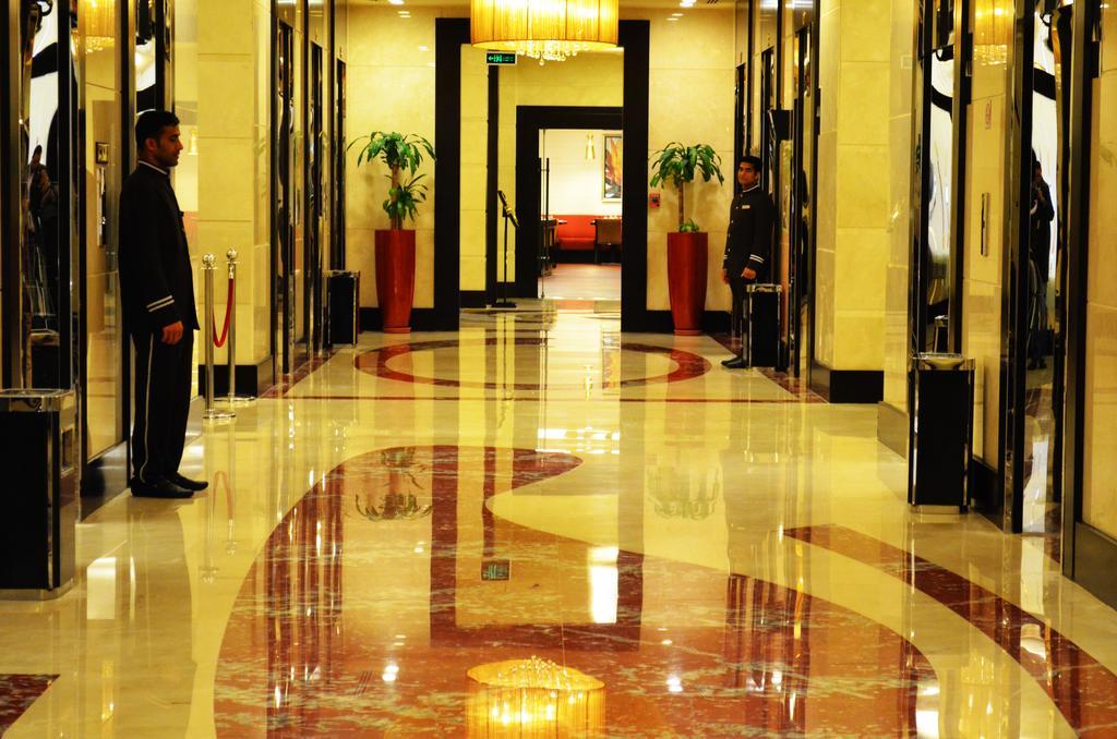 Al Ghufran Safwah Hotel Makkah Mekka Exteriör bild The photo shows an elegant hallway in a building, likely a hotel or a high-end establishment. The floor is made of polished marble with a decorative pattern. There are two doormen or attendants standing on either side of the hallway, each dressed in 